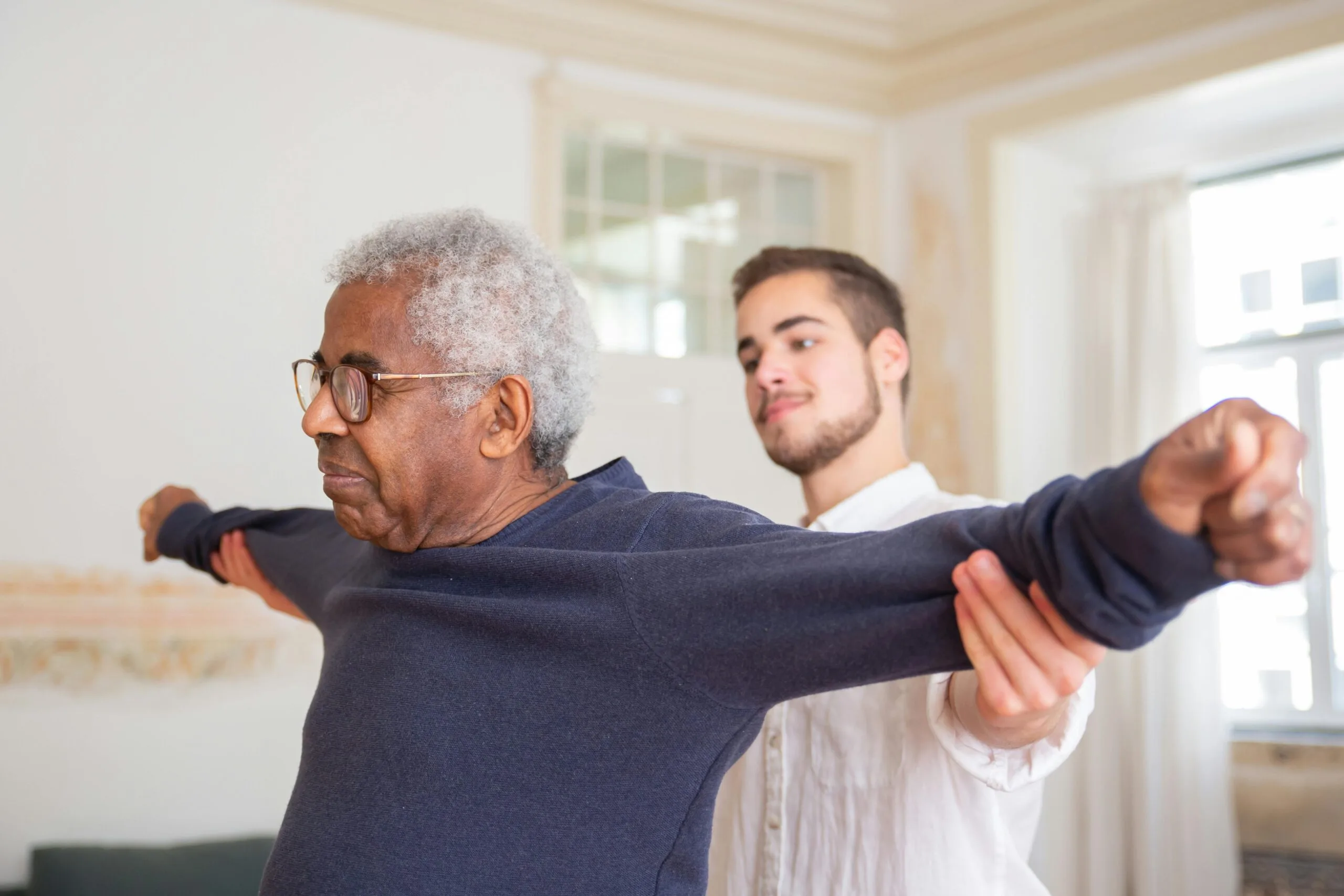A senior man is assisted by a StretchMaster Physiotherapist for stretching exercises indoors.