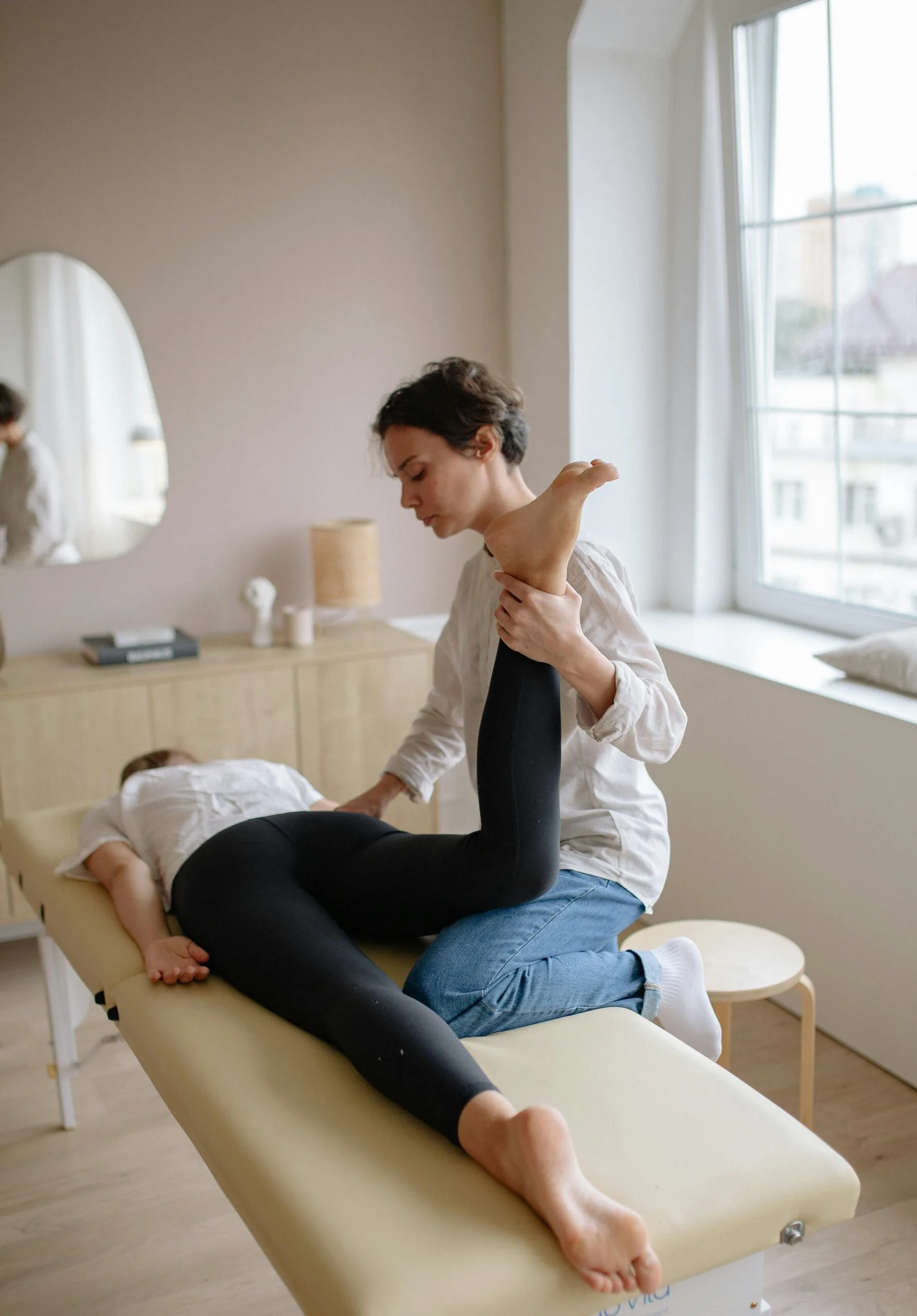A stretchMasters Physiotherapist aiding a woman with leg exercises on a massage table for relaxation and therapy.