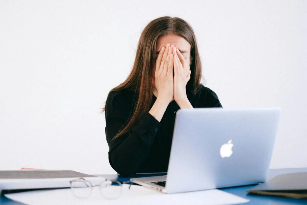 Woman feeling stressed and overwhelmed at her desk while working remotely on a laptop.