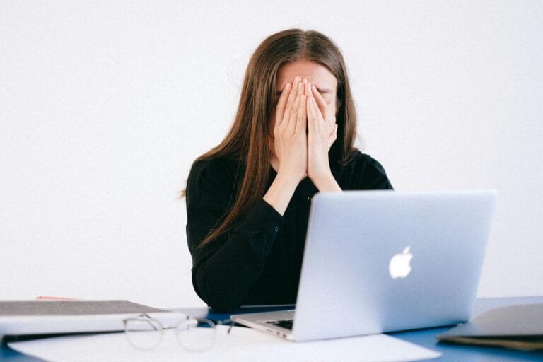 Woman feeling stressed and overwhelmed at her desk while working remotely on a laptop.