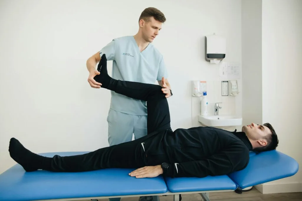 A StretchMasters physiotherapist assists a patient with leg stretching exercises on a treatment table.