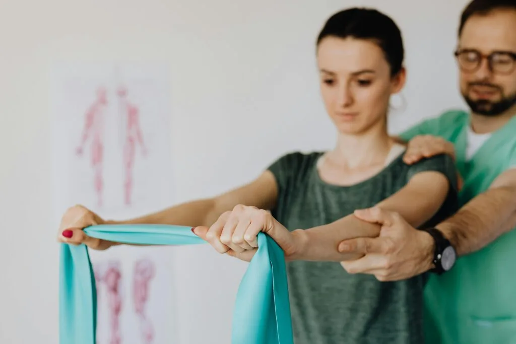 A young woman receives physical therapy assistance from a StretchMasters® therapist, using a stretching band for rehabilitation.