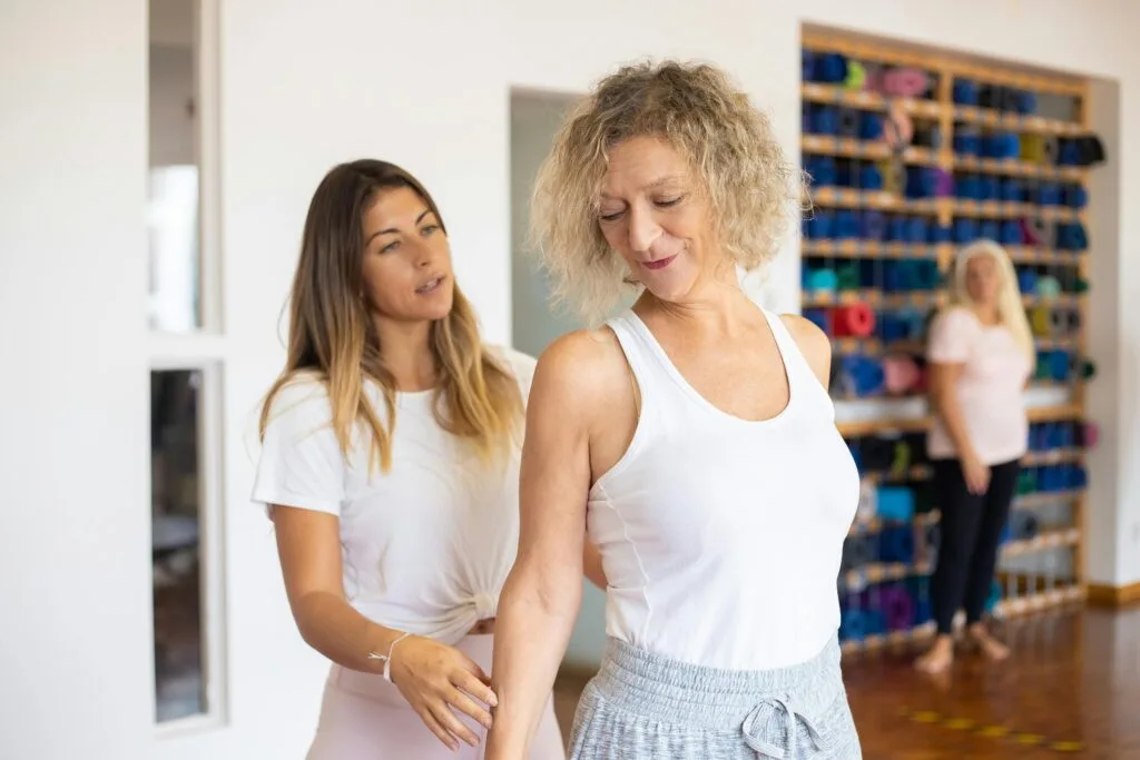 StretchMasters® therapist helping a client with exercise posture in a bright studio setting.