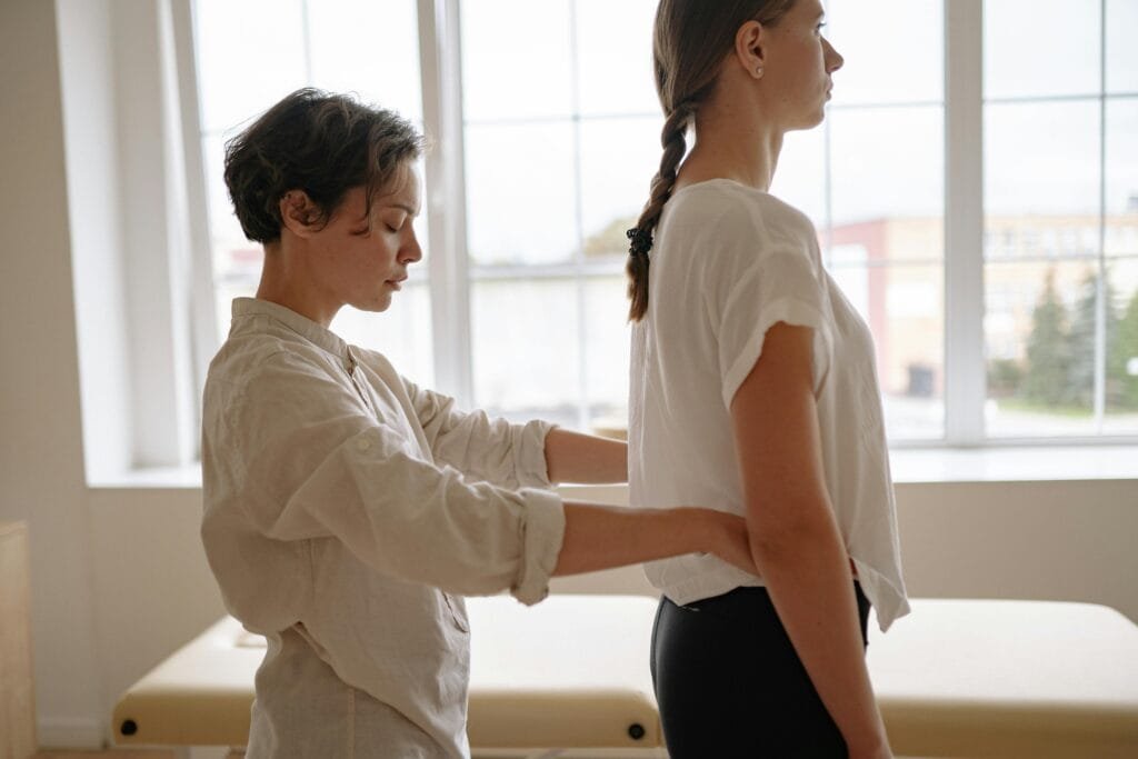 A professional therapist adjusting a standing woman indoors. Ideal for healthcare themes.