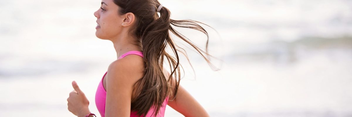pexels-photo-1199590-1199590 Side view of a young woman jogging on a beach wearing pink active wear.