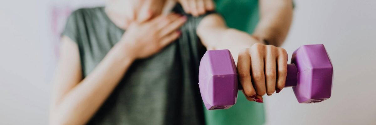 pexels-photo-4506078-4506078 Physiotherapist in uniform helping slender female in casual wear reaching arm with dumbbell in doctor office in hospital